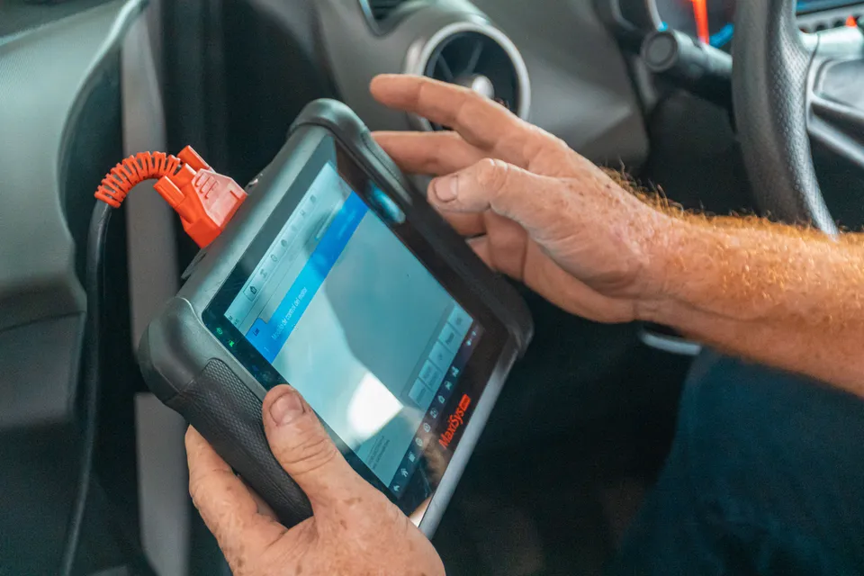 Technician holding a diagnostic scan tablet plugged into a car