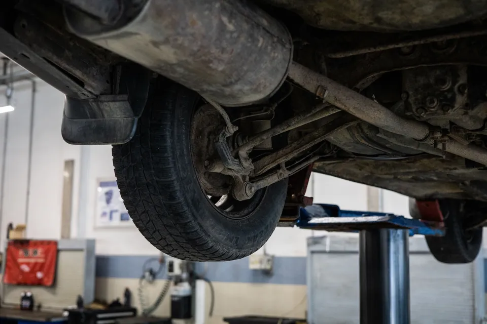 Underside of a car on a lift, showing a rear wheel and suspension parts